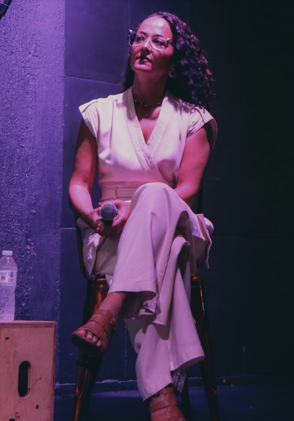 Luana Trindade sentada no palco, com o microfone nas mãos