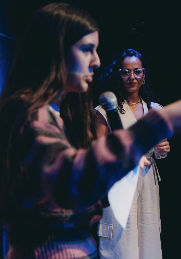 Uma participante fala ao microfone com Luana Trindade ao fundo