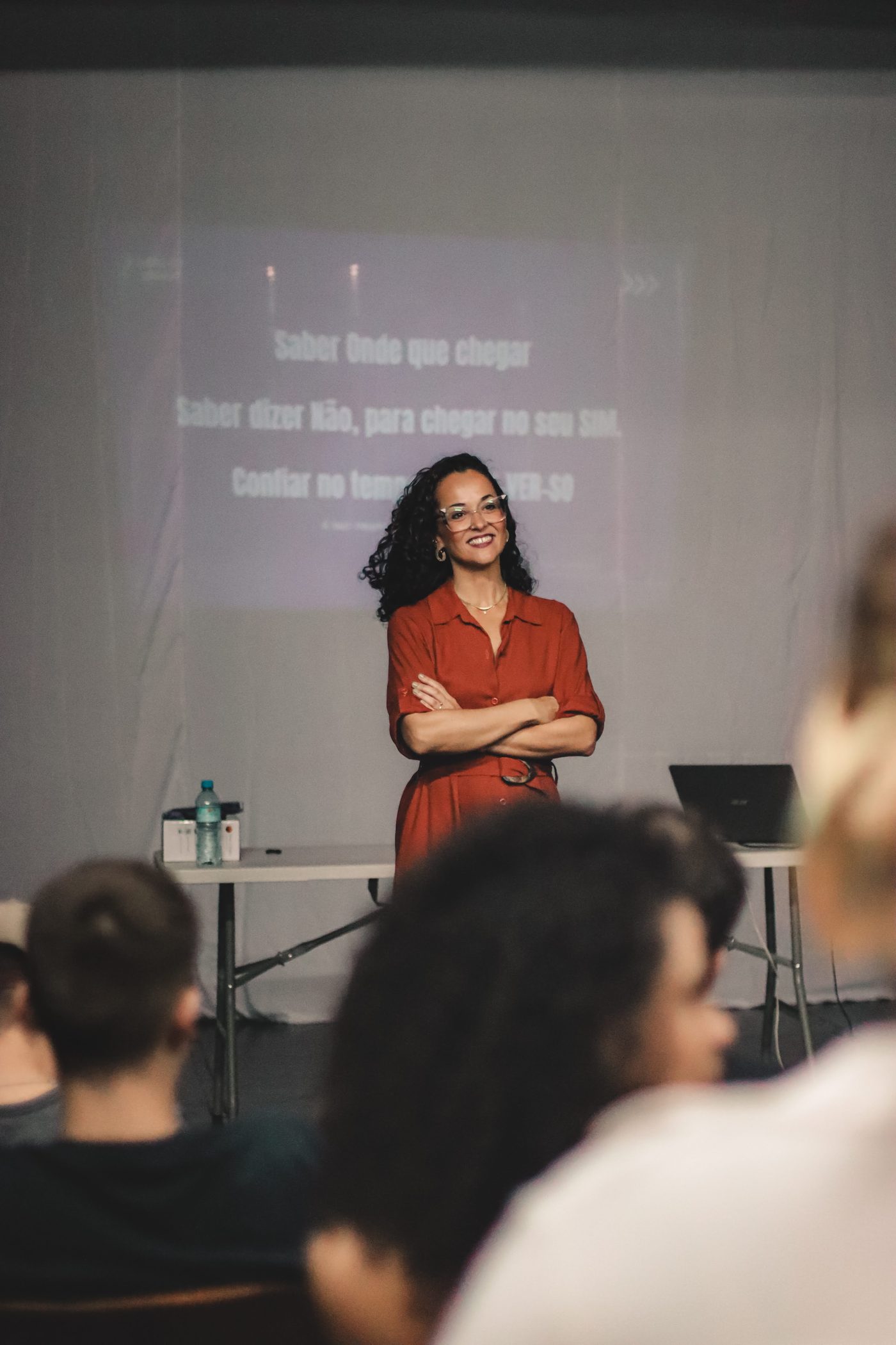 Luana Trindade de braços cruzados diante do slide da palestra